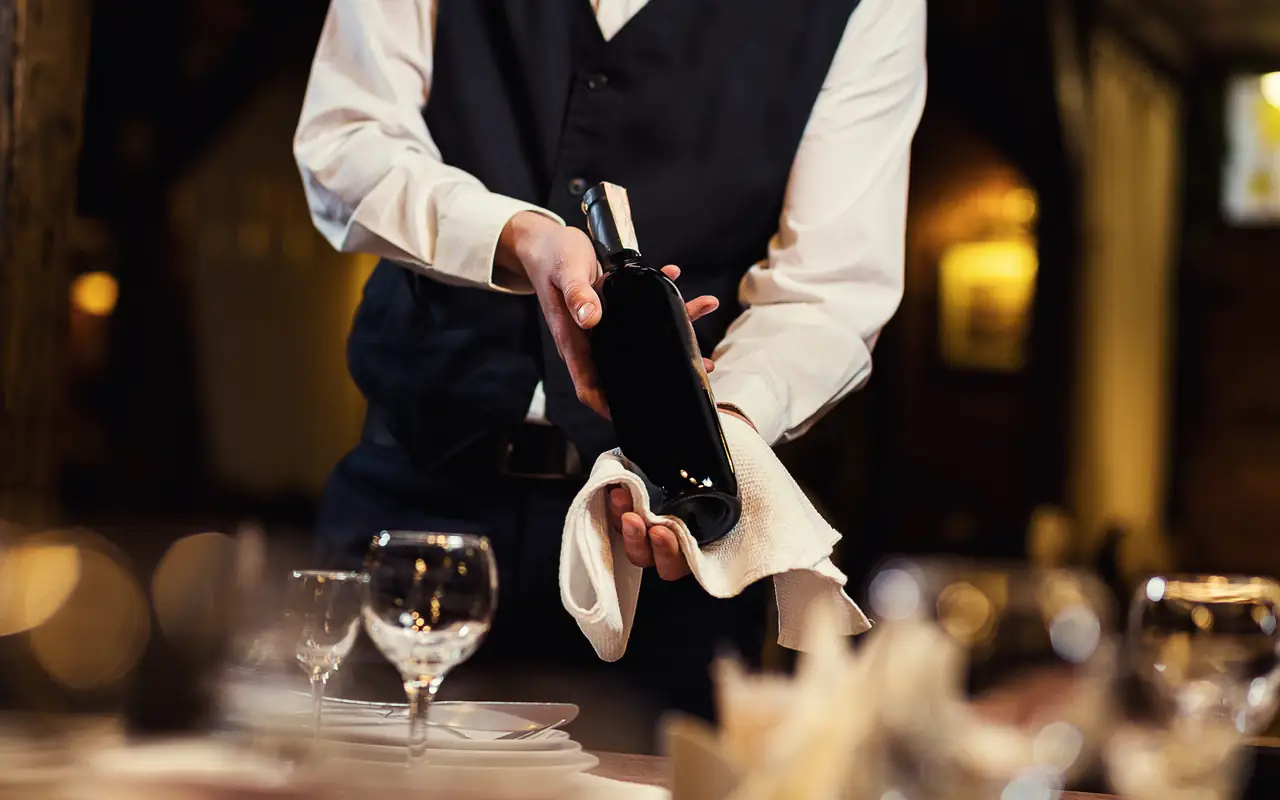 A server presenting a bottle of wine at a candlelit restaurant table